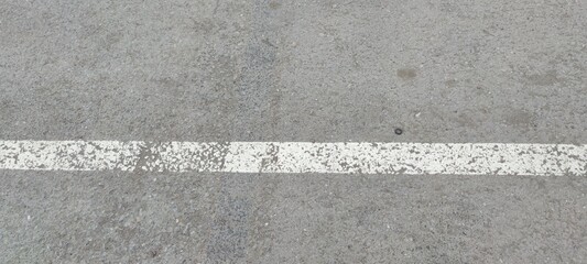 Fototapeta premium White stripe on gray asphalt. On light gray rough asphalt there is a light white stripe. The strip was applied in karsky, the paint was erased in places.