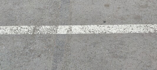 Fototapeta premium White stripe on gray asphalt. On light gray rough asphalt there is a light white stripe. The strip was applied in karsky, the paint was erased in places.