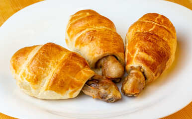 Appetizing chicken legs in puff pastry on a white plate and wooden background