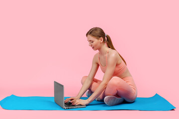 young sportive woman doing workout with laptop, on pink background, Fitness training online