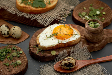 Fried eggs on a bun with black pepper and herbs on a wooden board.