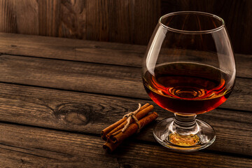 Glass of brandy with cinnamon sticks tied with jute rope on an old wooden table. Angle view