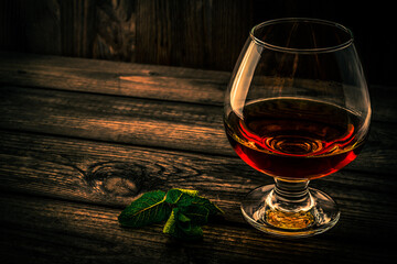 Glass of brandy with mint sprig on an old wooden table. Angle view