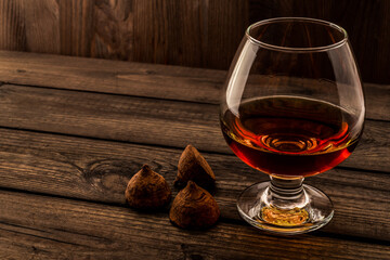 Glass of brandy and a chocolate truffles on an old wooden table. Angle view