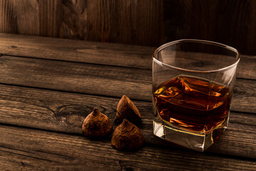Glass of brandy and a chocolate truffles on an old wooden table. Angle view