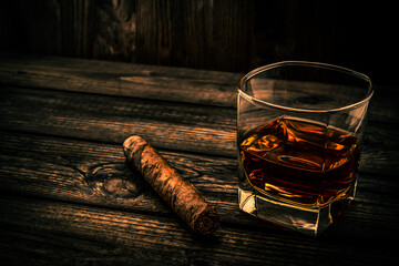 Glass of brandy and cuban cigar on an old wooden table. Angle view