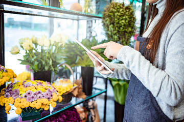People, business, technology, sale and floristry and concept - Florist woman with tablet pc computer at flower shop. Female florist working in flower shop with tablet - obrazy, fototapety, plakaty
