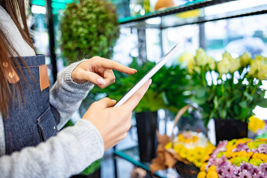 Beautiful female florist with tablet in flower shop. Young girl takes pictures of floral bouquets on a tablet. Young owner of flower shop taking orders online by tablet. Small business