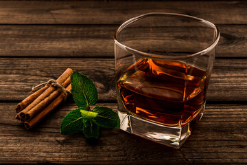 Glass of brandy with mint sprig and cinnamon sticks tied with jute rope on an old wooden table....
