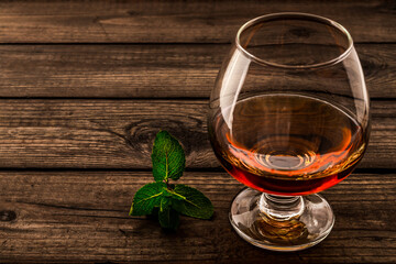 Glass of brandy with mint sprig on an old wooden table. Close up view