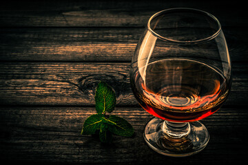 Glass of brandy with mint sprig on an old wooden table. Close up view