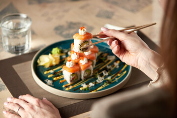 A dish of Japanese cuisine - seafood rolls. Woman's hand holds sticks with a roll