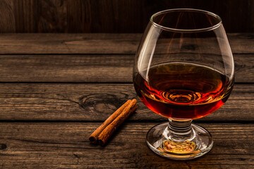 Glass of brandy with cinnamon stick on a wooden table. Angle view