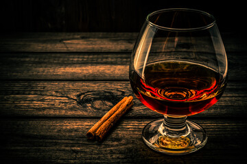 Glass of brandy with cinnamon stick on a wooden table. Angle view