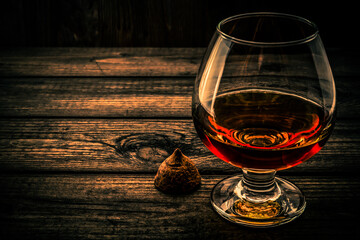 Glass of brandy and a chocolate truffle on an old wooden table. Angle view