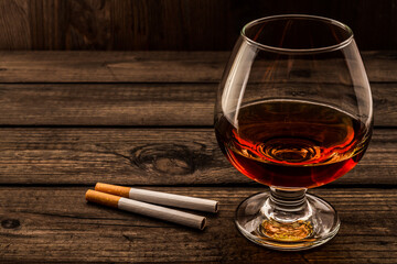 Glass of brandy with two cigarettes on a old wooden table. Angle view