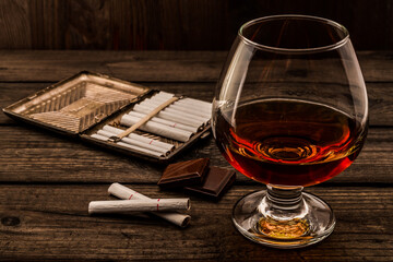 Glass of brandy and a chocolate with cigarette case on an old wooden table. Angle view