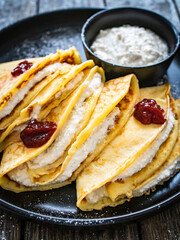 Sweet crepes stuffed with cream cottage cheese and strawberries jam on wooden table
