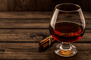 Glass of brandy with cinnamon sticks tied with jute rope on an old wooden table. Angle view