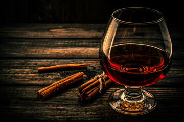 Glass of brandy with cinnamon sticks tied with jute rope on an old wooden table. Angle view