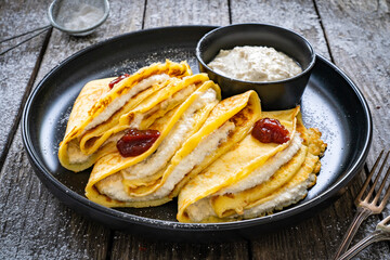 Sweet crepes stuffed with cream cottage cheese and strawberries jam on wooden table
