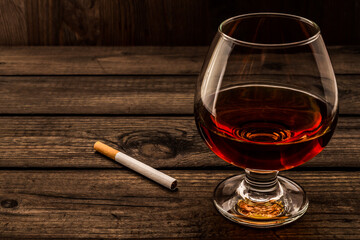 Glass of brandy and cigarette on a old wooden table. Angle view