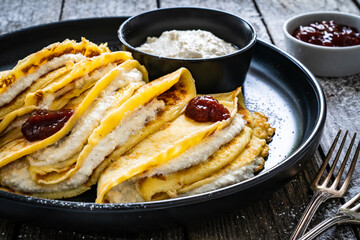 Sweet crepes stuffed with cream cottage cheese and strawberries jam on wooden table
