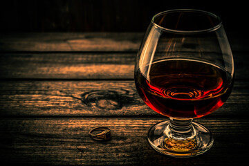 Glass of brandy and golden ring on an old wooden table. Angle view