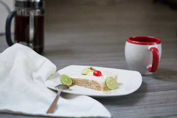 Lemon foot or lemon carlote on a white plate on a gray background accompanied with a cup of coffee