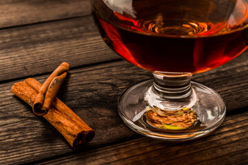 Glass of brandy with cinnamon stick on an old wooden table. Close up view