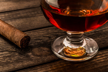 Glass of brandy and cuban cigar on an old wooden table. Close up view