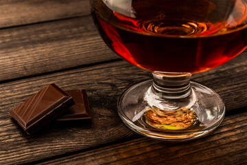 Glass of brandy and a chocolate on an old wooden table. Close up view