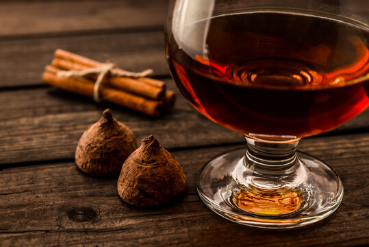 Glass of brandy and a couple of chocolate truffles with cinnamon sticks tied with jute rope on an old wooden table. Close up view, shallow depth of field