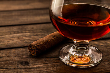 Glass of brandy and cuban cigar on an old wooden table. Close up view, shallow depth of field