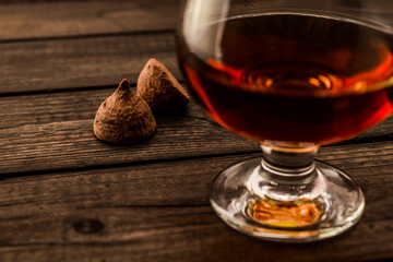 Glass of brandy and a couple of chocolate truffles on an old wooden table. Close up view, shallow depth of field, focus on the chocolate truffles