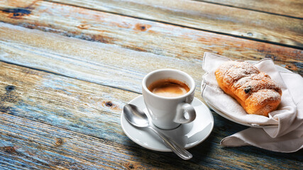 Cup of espresso coffee and brioche on an old wooden table.