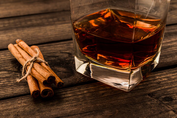 Glass of brandy with cinnamon sticks tied with jute rope on an old wooden table. Close up view
