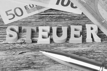 wooden letters with the German word 'Steuer' which means in English: tax, above are lying Euro banknotes