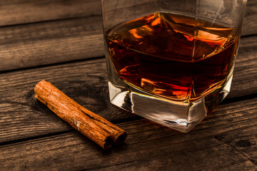 Glass of brandy with cinnamon stick on an old wooden table. Close up view