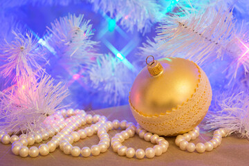 Golden glass Christmas bauble (decoration) with natural pearl garland (necklace) under the blue tinted Christmas tree with star shaped lights effect