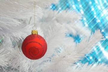 Red glass glitter ornament Christmas bauble (decoration) hanging on a white Christmas tree with star shaped lights effect