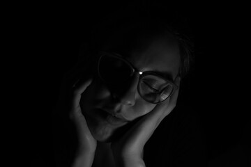 Dark low-key portrait of a middle-aged woman with glasses resting on a heavy hand after reading a document that can still be seen reflected in part of the glasses.