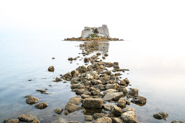 Stony path in a calm sea towards an old collapsed building. Long exposure.