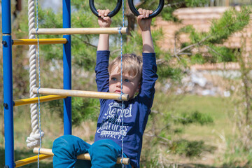 Obraz premium A blonde-haired child is playing on the playground, hanging on rings.