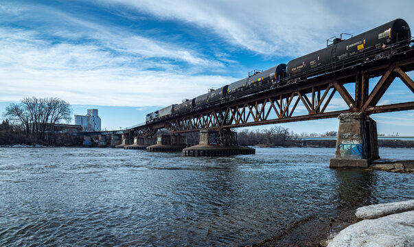 A train pulls oil cars over a bridge crossing the Mississippi river near Minneapolis Minnesota under blue skies