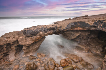 Fototapeta na wymiar Arch shaped rock formation in the coastline at the sunset. Long exposure