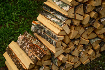 Birch firewood is lying on the green grass. A fire of wood. Harvesting firewood for the winter in the summer in the village. Fuel for the stove. Felled forest. Birch bark.