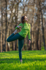 Athletic sportive girl in park on green grass doing fitness exercises stretching the body, healthy lifestyle in pure nature