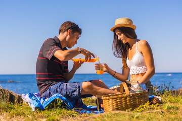 A young man serving his girlfriend orange juice in the mountains by the sea enjoying the heat, summer lifestyle