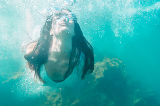A young Caucasian brunette in a white dress inside the sea, underwater image, summer lifestyle